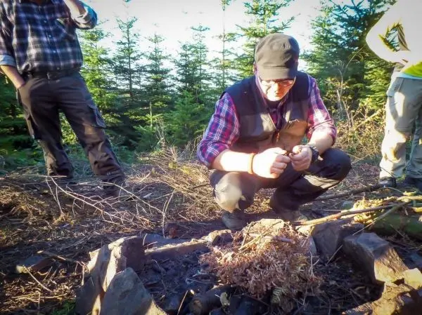 Mann zündet Zunder in einer Feuerstelle mit Steinen an
