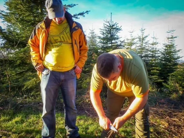 Messer schneidet Holzstück auf dem Boden, während eine Person zuschaut