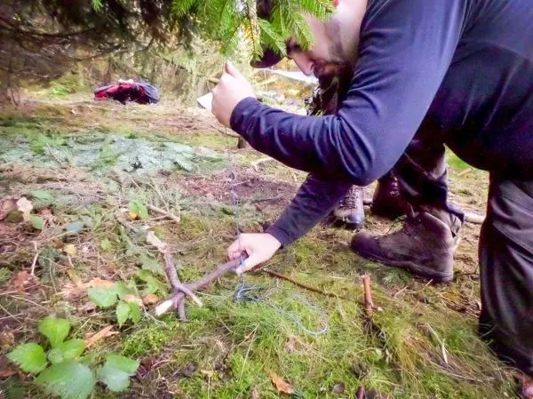 Messer schneidet Schnur für eine selbstgebaute Schlagfalle auf dem Waldboden