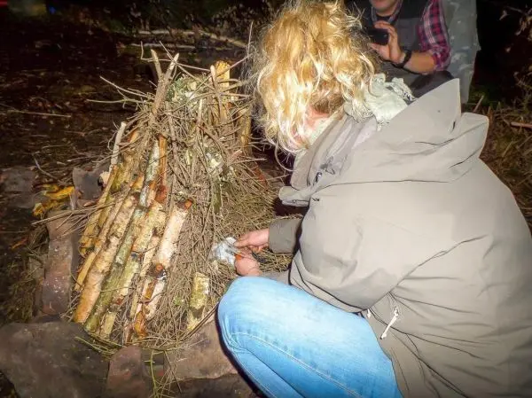 Person baut ein Feuer mit Zweigen und trockenem Material beim Survival Training
