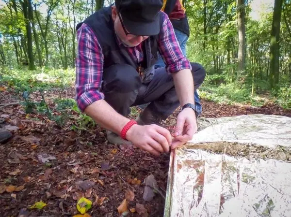 Person befestigt eine reflektierende Notunterkunft im Wald