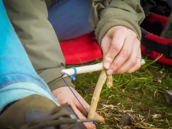 Person bindet Holzstücke mit Schnur zusammen