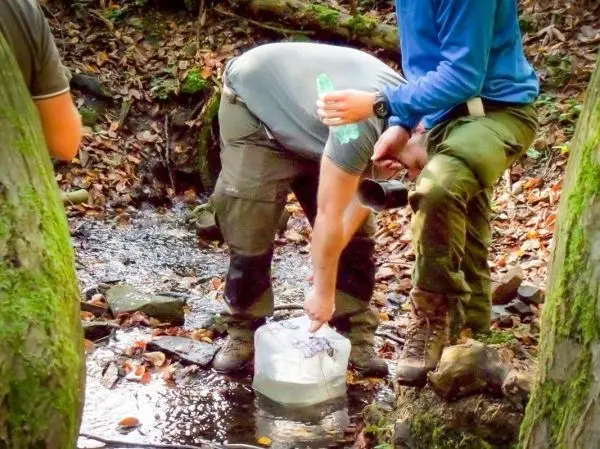 Person füllt Wasser in einen Behälter aus einem Bach beim Survival Training
