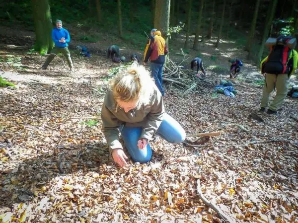 Person kniet im Laub und untersucht den Boden im Wald