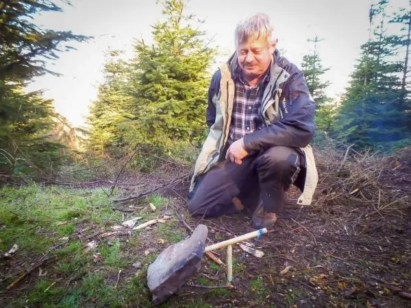 Person kniet neben einem Stein mit Holzstöcken im Wald