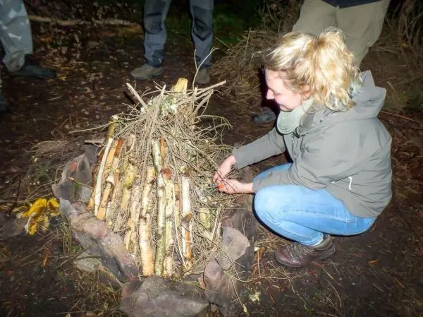 Person legt Äste auf einen Holzstapel beim Feuer machen