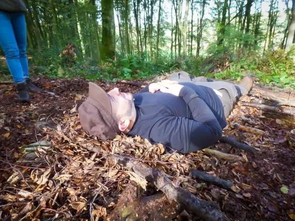 Person liegt auf dem Boden im Wald zwischen Ästen und Laub