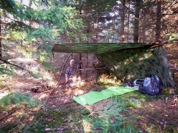 Person sitzt unter einer selbstgebauten Plane im Wald
