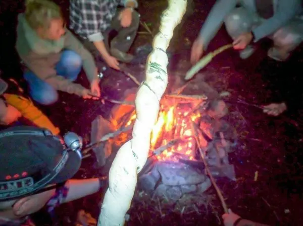 Personen halten Stöcke über ein Feuer beim Überlebenstraining