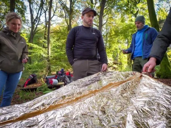 Personen um eine reflektierende Notunterkunft versammelt, einer hält die Kante fest