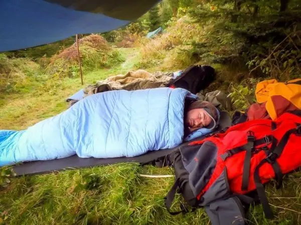 Schlafsack liegt auf Isomatte, umgeben von Rucksäcken und Decken