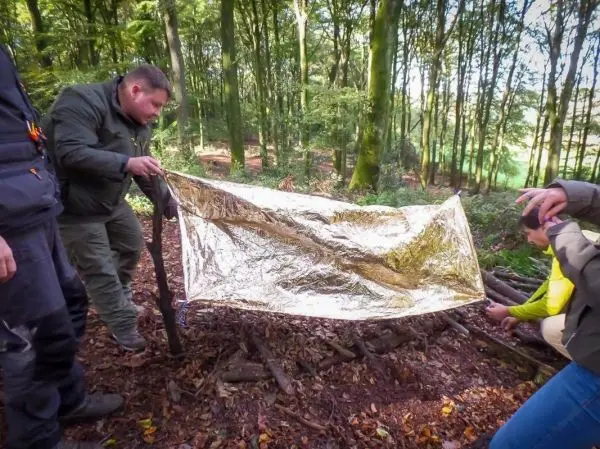 Tarp-Notunterkunft wird mit einer reflektierenden Folie über einer Holzstruktur befestigt