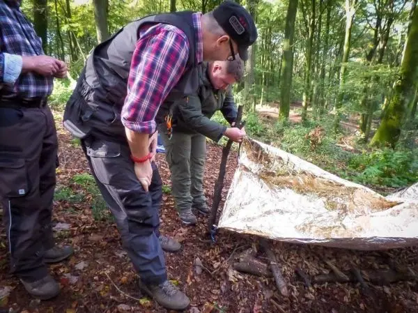 Tarp-Notunterkunft wird mit Stöcken und Schnüren aufgebaut