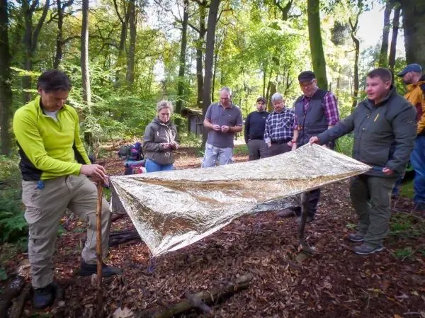 Zwei Personen halten eine reflektierende Notunterkunft aus Folie in einem Wald