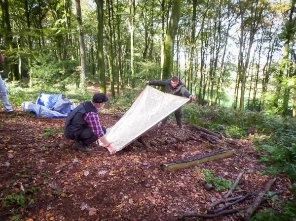 Zwei Personen spannen eine Tarp-Notunterkunft zwischen Holzstücken auf