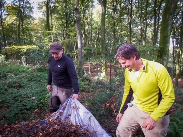 Zwei Personen tragen eine Plane mit Laub durch den Wald