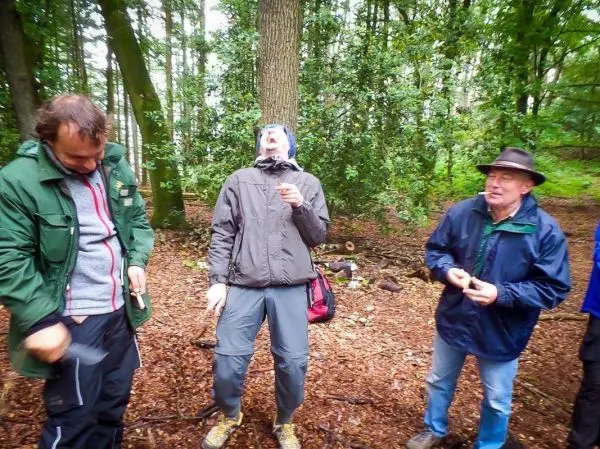 Drei Personen stehen im Wald und interagieren miteinander, während eine Person etwas in der Hand hält