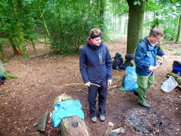 Frau hält Stock über einem Holzstück, Mann bereitet Ausrüstung am Boden vor