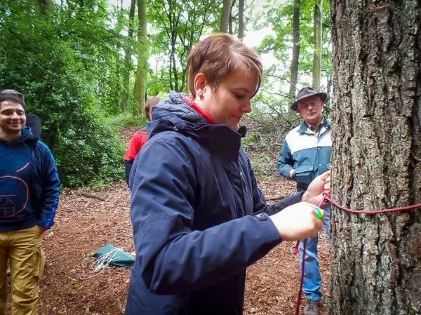 Frau knotet ein Seil an einen Baumstamm im Wald