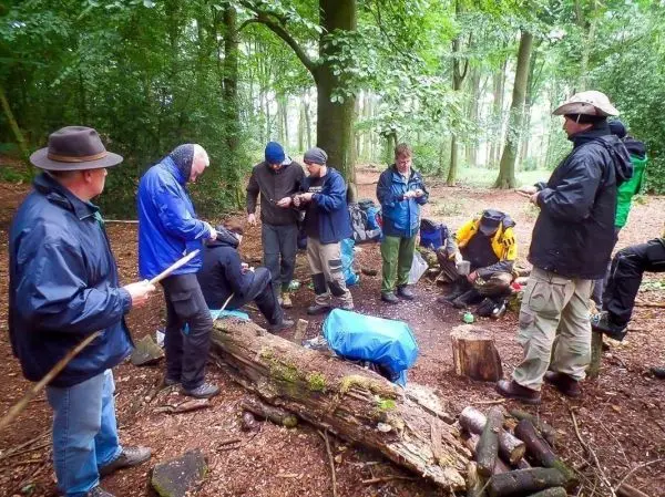 Gruppe arbeitet an einer Holzstruktur im Wald, Ausrüstung und Materialien liegen verstreut