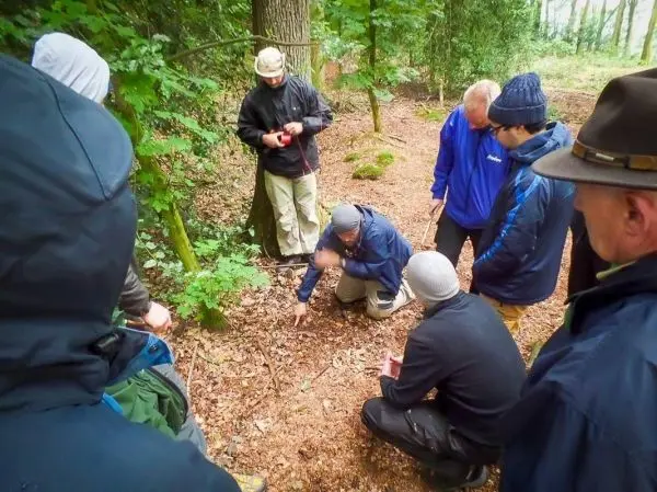 Gruppe betrachtet den Boden im Wald, während jemand eine Technik demonstriert