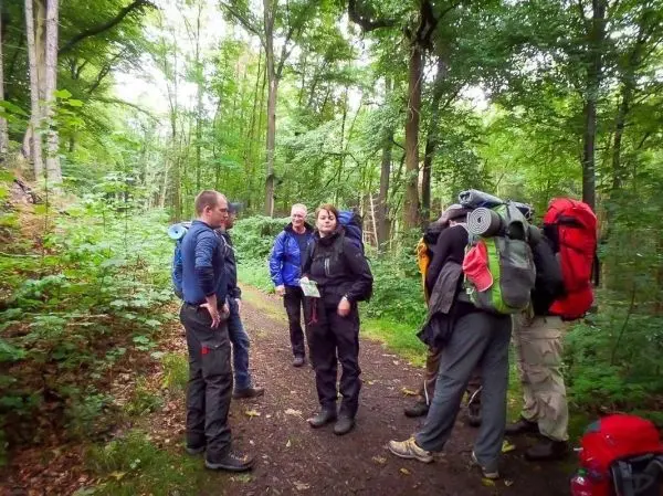 Gruppe mit Rucksäcken steht auf einem Waldweg und bespricht sich