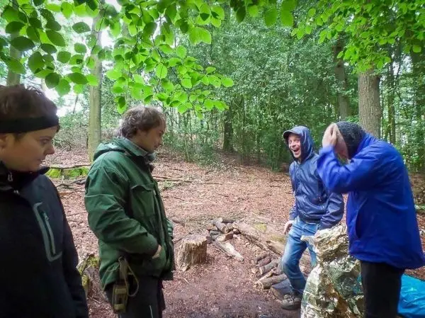 Gruppe steht im Wald, einer hält eine reflektierende Folie, andere lachen