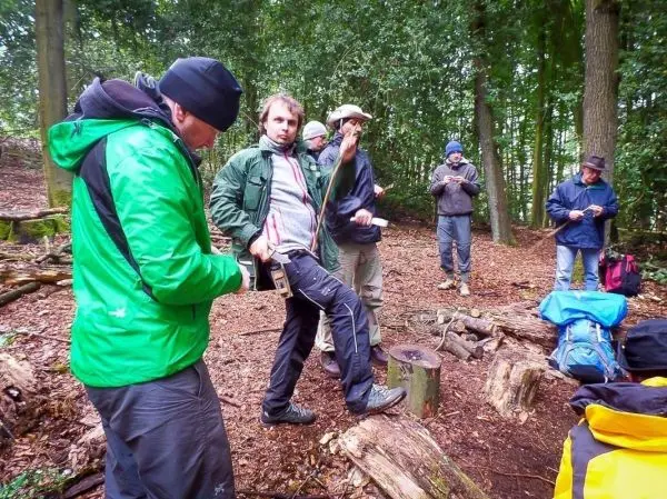 Gruppe von Personen steht im Wald und betrachtet Ausrüstung beim Überlebenstraining