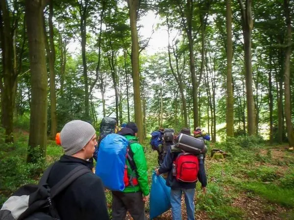 Gruppe von Personen wandert mit Rucksäcken durch den Wald beim Überlebenstraining