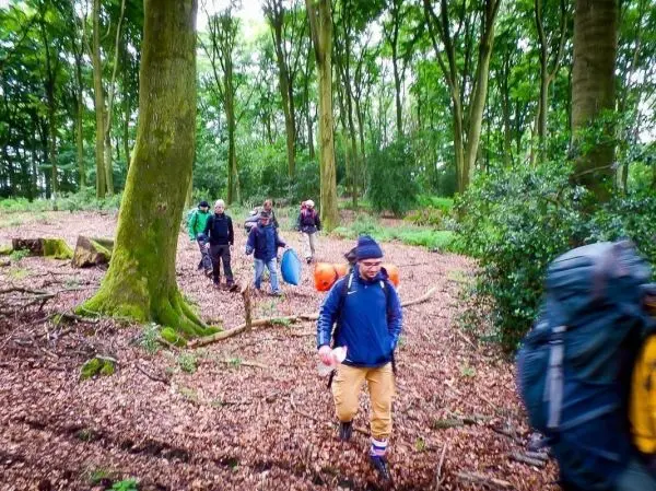 Gruppe wandert mit Rucksäcken durch einen bewaldeten Bereich mit Laub