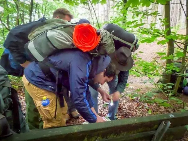 Gruppierung betrachtet Karte auf dem Boden im Wald, Rucksäcke auf dem Rücken