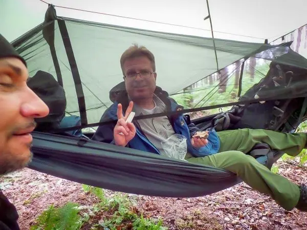 Hängematte zwischen Bäumen mit Person, die Snack hält und Peace-Zeichen zeigt