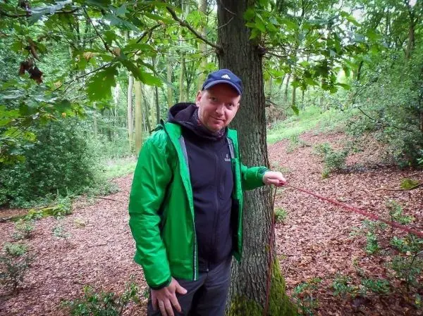 Mann hält ein Seil neben einem Baum im Wald
