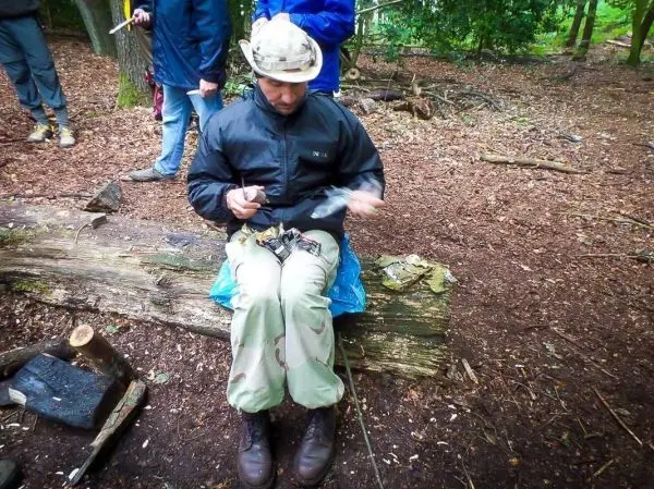 Mann sitzt auf einem Baumstamm und schnitzt mit einem Messer
