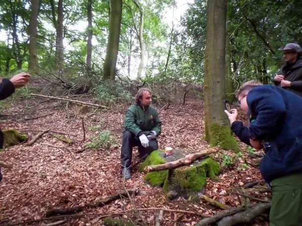 Mann sitzt auf einem Baumstumpf im Wald, während andere ihn fotografieren
