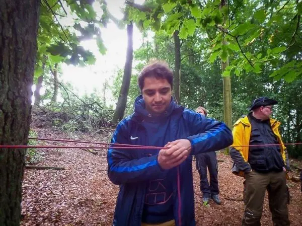 Mann spannt ein rotes Seil zwischen zwei Bäumen im Wald