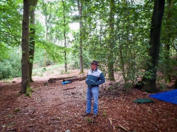 Mann steht in einem Waldgebiet mit Laub und Bäumen, Tarp im Hintergrund