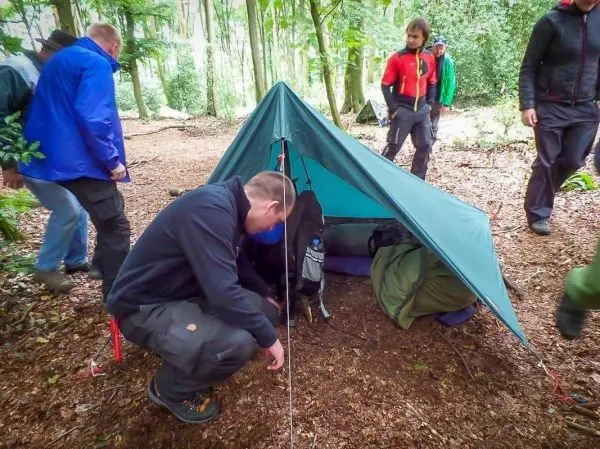 Mann überprüft die Abspannung einer Tarp-Notunterkunft im Wald