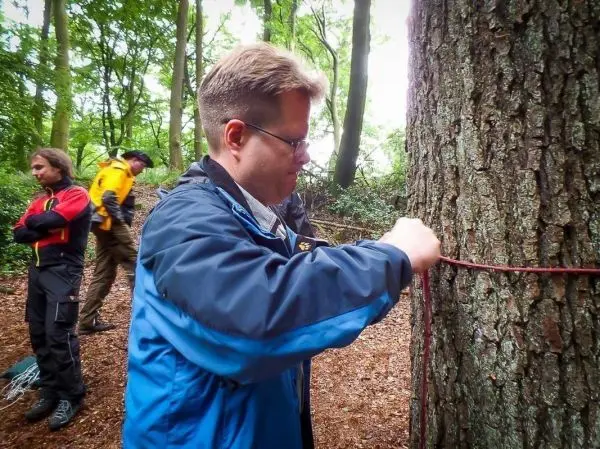 Person bindet ein Seil um einen Baum