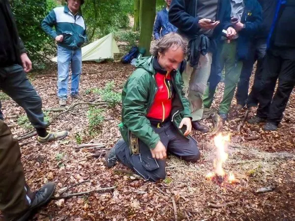 Person kniet vor einem kleinen Feuer im Wald