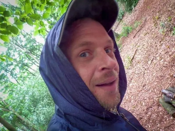 Person mit Kapuze schaut in die Kamera im Wald