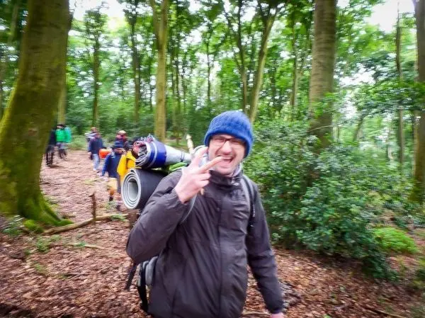 Person zeigt Peace-Zeichen und trägt Rucksack im Wald