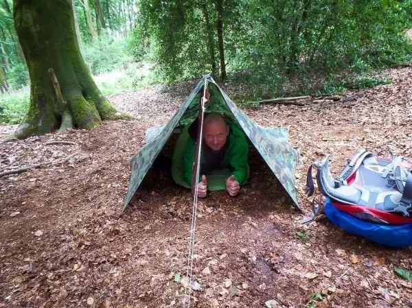 Tarp-Notunterkunft aus Plane mit Person, die darin sitzt und Daumen hoch zeigt