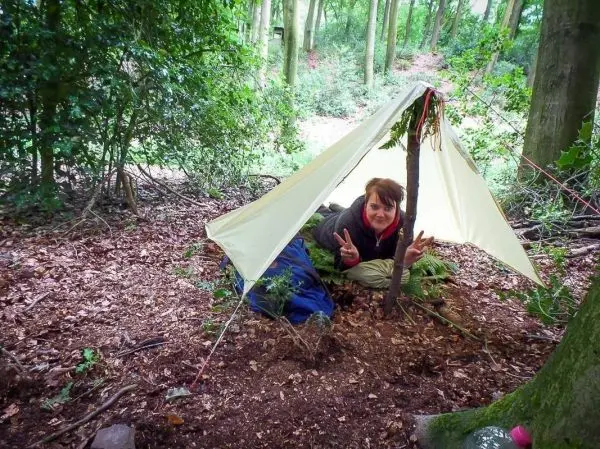Tarp-Notunterkunft mit einem Baumstamm als Stütze im Wald aufgebaut