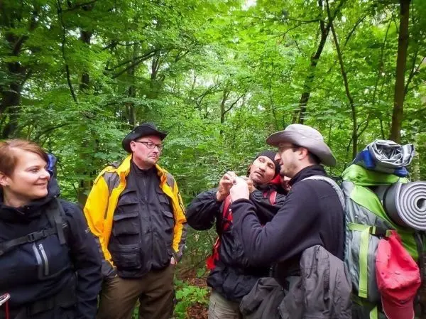 Vier Personen mit Rucksäcken stehen im Wald und diskutieren