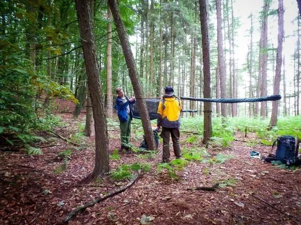 Zwei Personen bauen eine Tarp-Notunterkunft zwischen zwei Bäumen auf