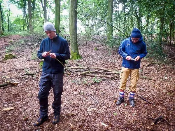 Zwei Personen bearbeiten Äste im Wald, um Zunder oder Werkzeuge herzustellen