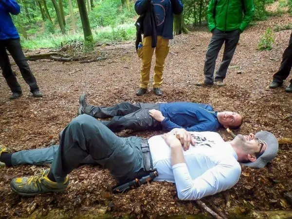 Zwei Personen liegen auf dem Waldboden, umgeben von anderen Teilnehmern
