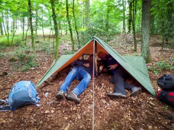 Zwei Personen sitzen unter einem grünen Tarp im Wald