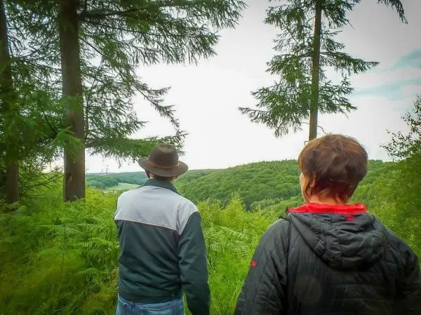 Zwei Personen stehen im Wald und blicken auf eine bewaldete Landschaft